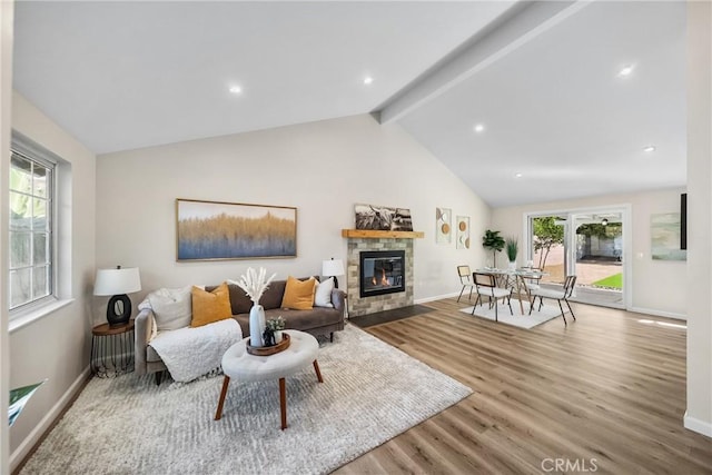 living room featuring baseboards, a stone fireplace, wood finished floors, and vaulted ceiling with beams