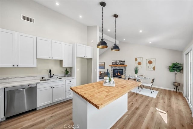 kitchen with visible vents, a stone fireplace, white cabinets, wood counters, and stainless steel dishwasher