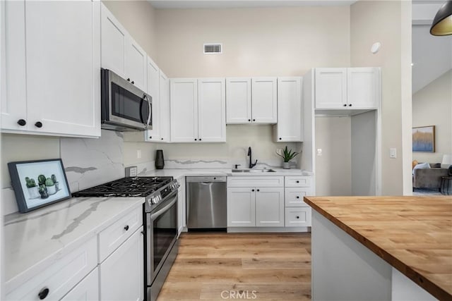 kitchen with a sink, white cabinetry, appliances with stainless steel finishes, and butcher block countertops