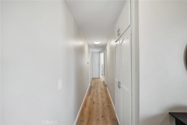 hallway featuring light wood-style flooring, attic access, and baseboards