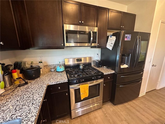 kitchen featuring light wood finished floors, light stone countertops, and appliances with stainless steel finishes