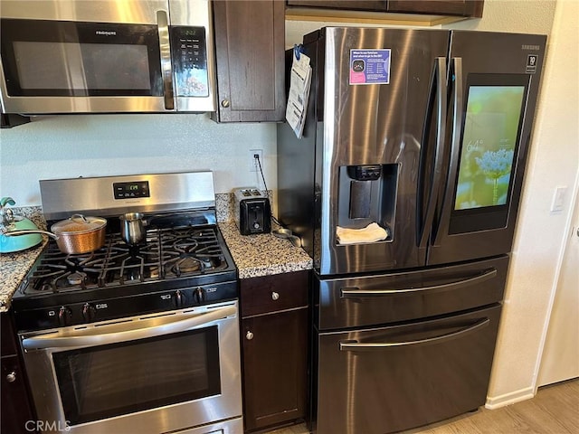 kitchen featuring light wood-type flooring, appliances with stainless steel finishes, light stone countertops, dark brown cabinets, and a textured wall