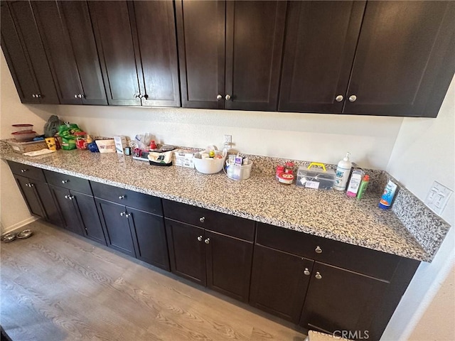 kitchen featuring dark brown cabinetry, light stone counters, and light wood-style floors