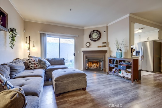 living room with wood finished floors, ornamental molding, and a glass covered fireplace
