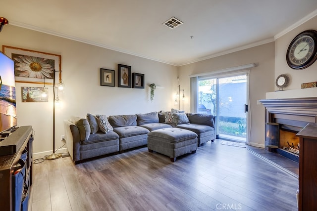 living room featuring wood finished floors, a fireplace, ornamental molding, and visible vents