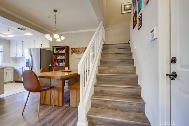 stairs featuring a chandelier, visible vents, ornamental molding, and wood finished floors