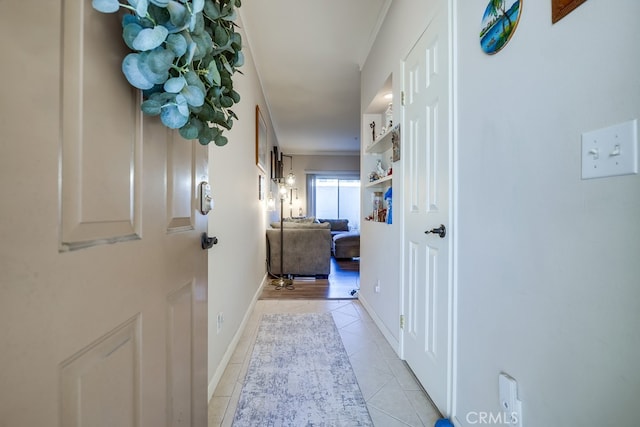 hallway featuring light tile patterned floors, baseboards, and ornamental molding