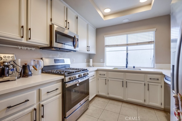 kitchen featuring light tile patterned floors, a raised ceiling, a sink, light countertops, and appliances with stainless steel finishes