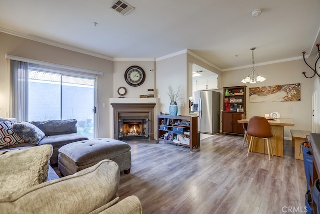 living area featuring an inviting chandelier, ornamental molding, a warm lit fireplace, visible vents, and light wood finished floors