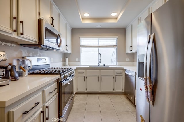 kitchen with a sink, light countertops, appliances with stainless steel finishes, a tray ceiling, and light tile patterned flooring