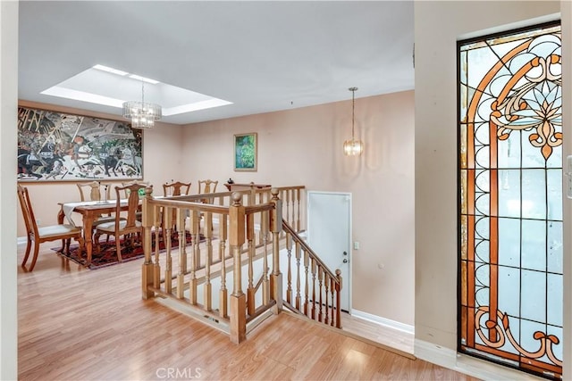 staircase featuring a raised ceiling, wood finished floors, baseboards, and a chandelier