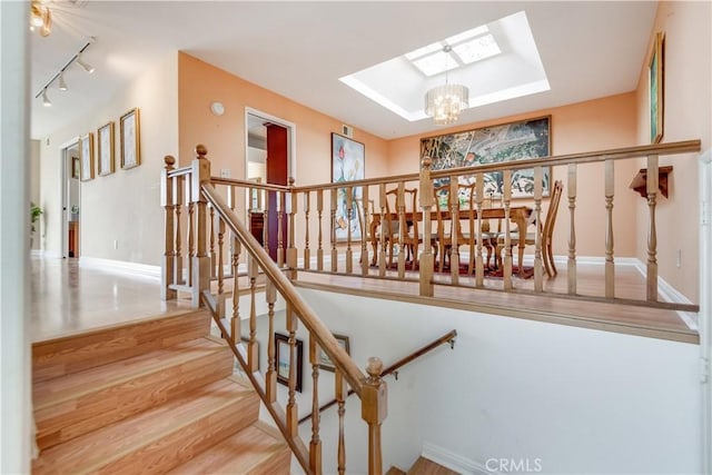 stairway with baseboards, wood finished floors, an inviting chandelier, and a skylight