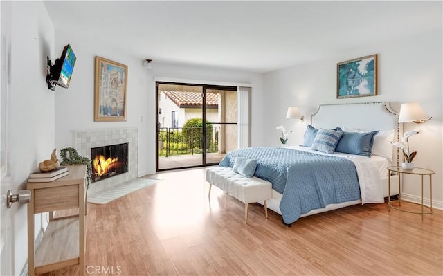 bedroom with wood finished floors, a tile fireplace, and access to outside