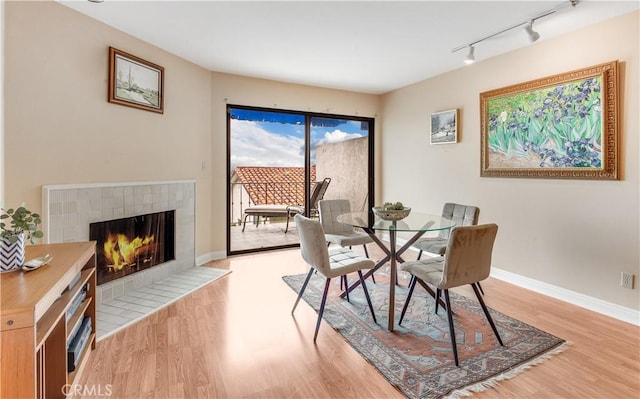 dining area with rail lighting, baseboards, light wood-style floors, and a fireplace