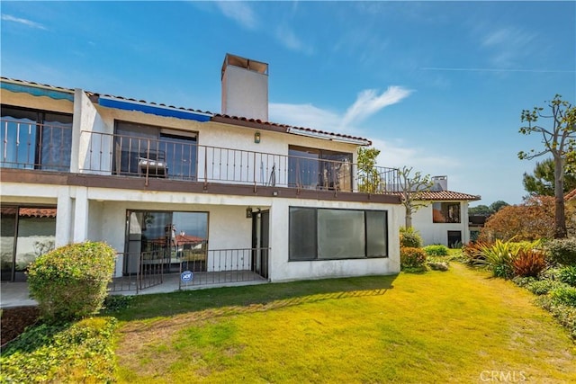 back of property featuring stucco siding, a yard, a balcony, and a chimney