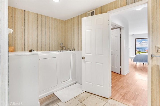 full bath featuring visible vents, a tub, wallpapered walls, wood finished floors, and washer / clothes dryer