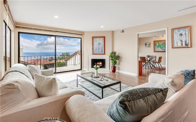 living area featuring visible vents, baseboards, recessed lighting, a warm lit fireplace, and wood finished floors