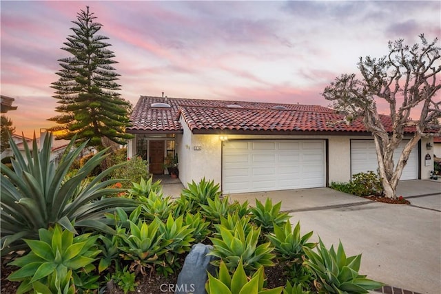 mediterranean / spanish house featuring stucco siding, concrete driveway, an attached garage, and a tile roof