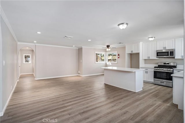 kitchen with light wood-type flooring, arched walkways, appliances with stainless steel finishes, white cabinets, and light countertops