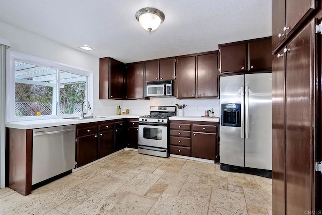 kitchen with a sink, stone tile floors, appliances with stainless steel finishes, light countertops, and dark brown cabinets