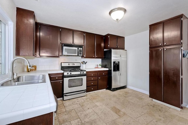 kitchen with dark brown cabinets, baseboards, tile countertops, appliances with stainless steel finishes, and a sink