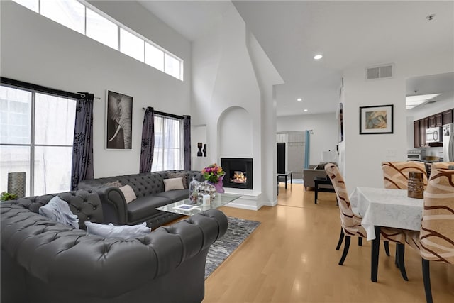 living area with visible vents, a high ceiling, recessed lighting, a multi sided fireplace, and light wood-type flooring