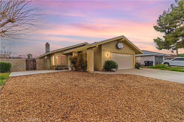 view of front of home with stucco siding, an attached garage, concrete driveway, and fence