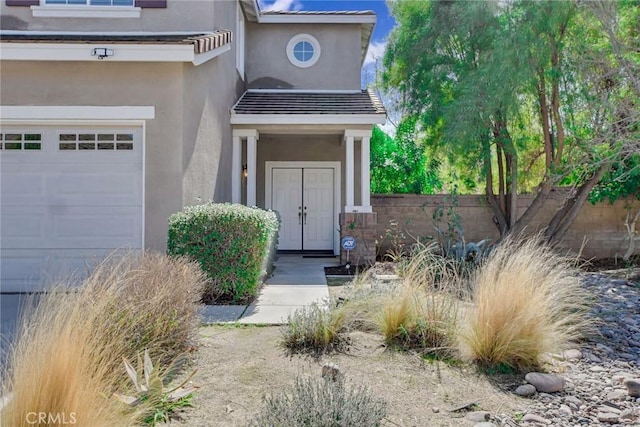 entrance to property featuring a tiled roof, an attached garage, fence, and stucco siding