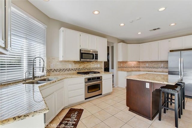 kitchen with visible vents, light stone counters, stainless steel appliances, white cabinetry, and a sink