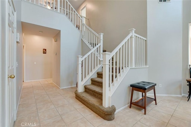 stairway with tile patterned floors, visible vents, a high ceiling, and baseboards