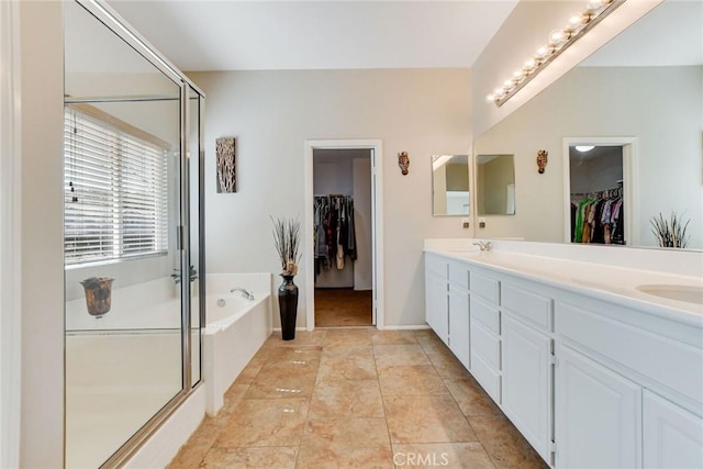 bathroom featuring a spacious closet, a shower stall, a garden tub, and double vanity