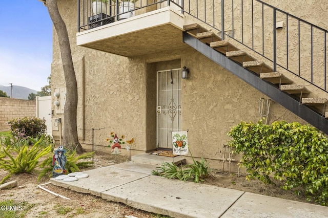 entrance to property with a balcony, stucco siding, and fence