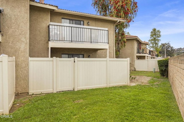 rear view of property with a tile roof, stucco siding, a fenced backyard, a balcony, and a lawn