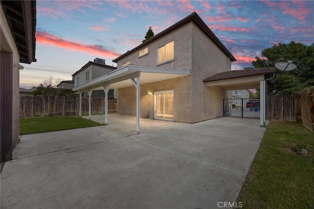 back of house at dusk with stucco siding, a patio, a lawn, and a fenced backyard