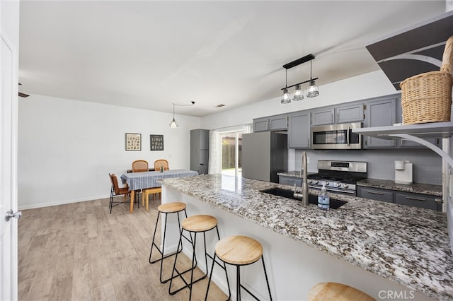 kitchen featuring a breakfast bar, a sink, stainless steel appliances, light wood finished floors, and light stone countertops