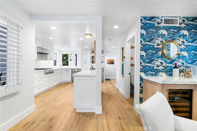 kitchen with under cabinet range hood, a sink, stainless steel appliances, light wood-style floors, and white cabinets