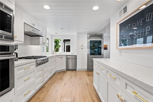 kitchen featuring light wood-type flooring, under cabinet range hood, tasteful backsplash, stainless steel appliances, and white cabinets