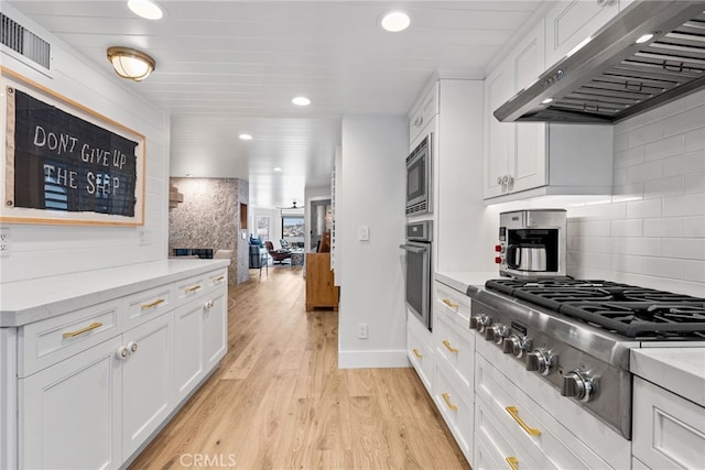 kitchen featuring visible vents, backsplash, light wood-style floors, exhaust hood, and stainless steel appliances