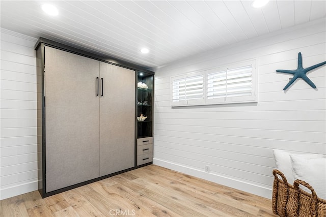 unfurnished bedroom with light wood-style flooring, recessed lighting, a closet, wood walls, and baseboards