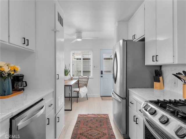 kitchen featuring light stone counters, stainless steel appliances, a ceiling fan, and white cabinetry