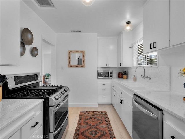 kitchen with visible vents, a sink, decorative backsplash, appliances with stainless steel finishes, and white cabinetry