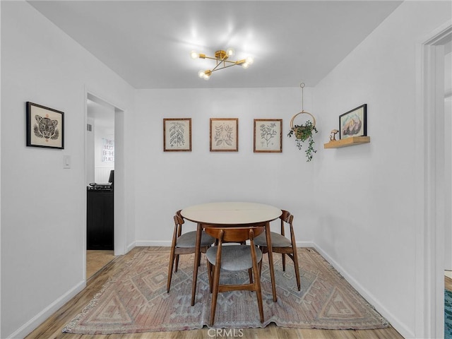 dining room with a notable chandelier, baseboards, and light wood-type flooring