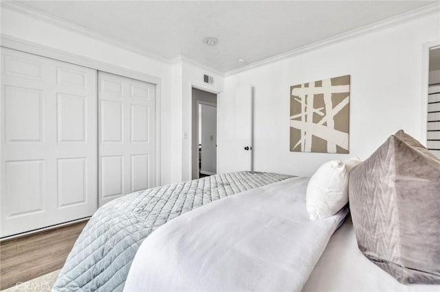 bedroom with a closet, visible vents, crown molding, and wood finished floors