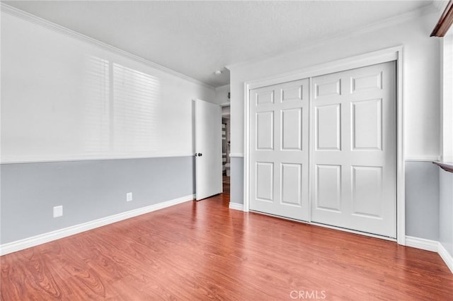 unfurnished bedroom with a closet, baseboards, wood finished floors, and ornamental molding