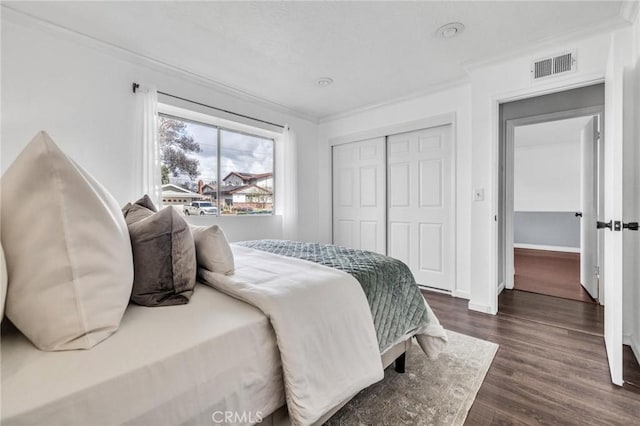 bedroom featuring dark wood-style floors, baseboards, visible vents, ornamental molding, and a closet