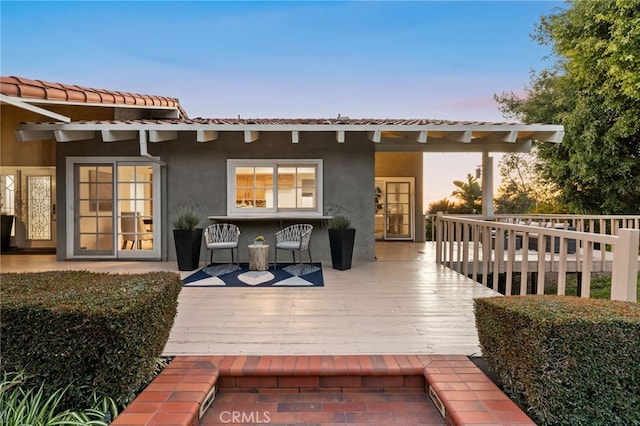 back of property at dusk with a wooden deck, a tiled roof, and stucco siding