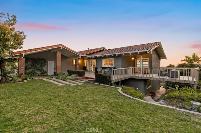 back of house featuring stucco siding, a yard, a deck, and a tiled roof