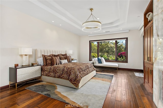 bedroom featuring a tray ceiling, dark wood-style floors, and baseboards