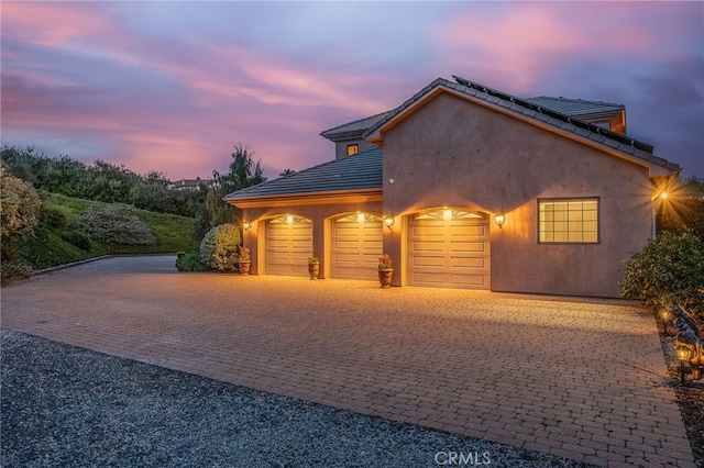 view of front facade featuring stucco siding, decorative driveway, roof mounted solar panels, a garage, and a tiled roof