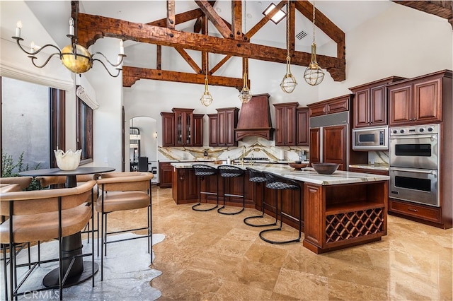 kitchen featuring arched walkways, decorative backsplash, built in appliances, custom exhaust hood, and a large island with sink